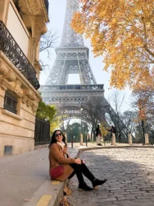 Woman sitting on a cobbled Paris street with the Eiffel Tower framed by autumn trees