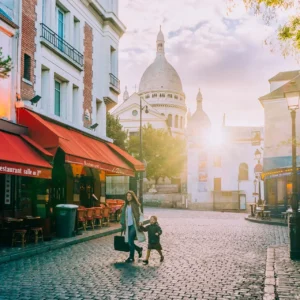 Woman and child crossing a quiet Montmartre street at sunrise with Sacré-Cœur in the background