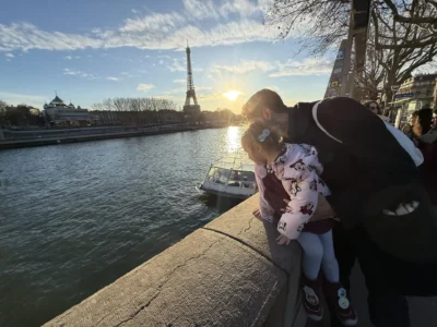 Father and child at the Seine embankment watching golden-hour light with the Eiffel Tower in the distance