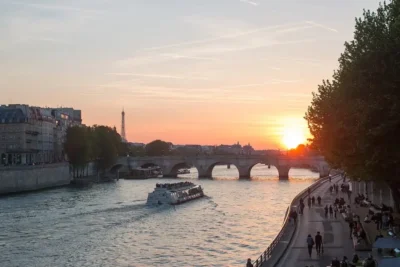 Tour boat on the Seine at sunset with a stone bridge and the Eiffel Tower in the distance